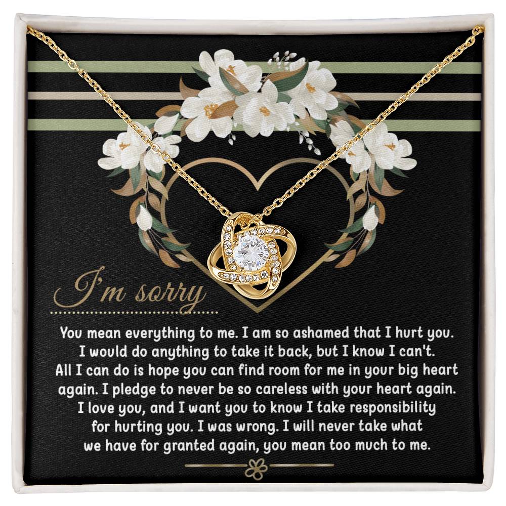 Introducing the Sorry-Big Heart - Love Knot Necklace: a heart-shaped pendant nestled in an elegant box, complete with an apology message expressing love and regret for causing hurt. The backdrop showcases a beautiful floral heart design, while the pendant sparkles with cubic zirconia crystals. Personalize your necklace by choosing between a white gold or yellow gold finish.