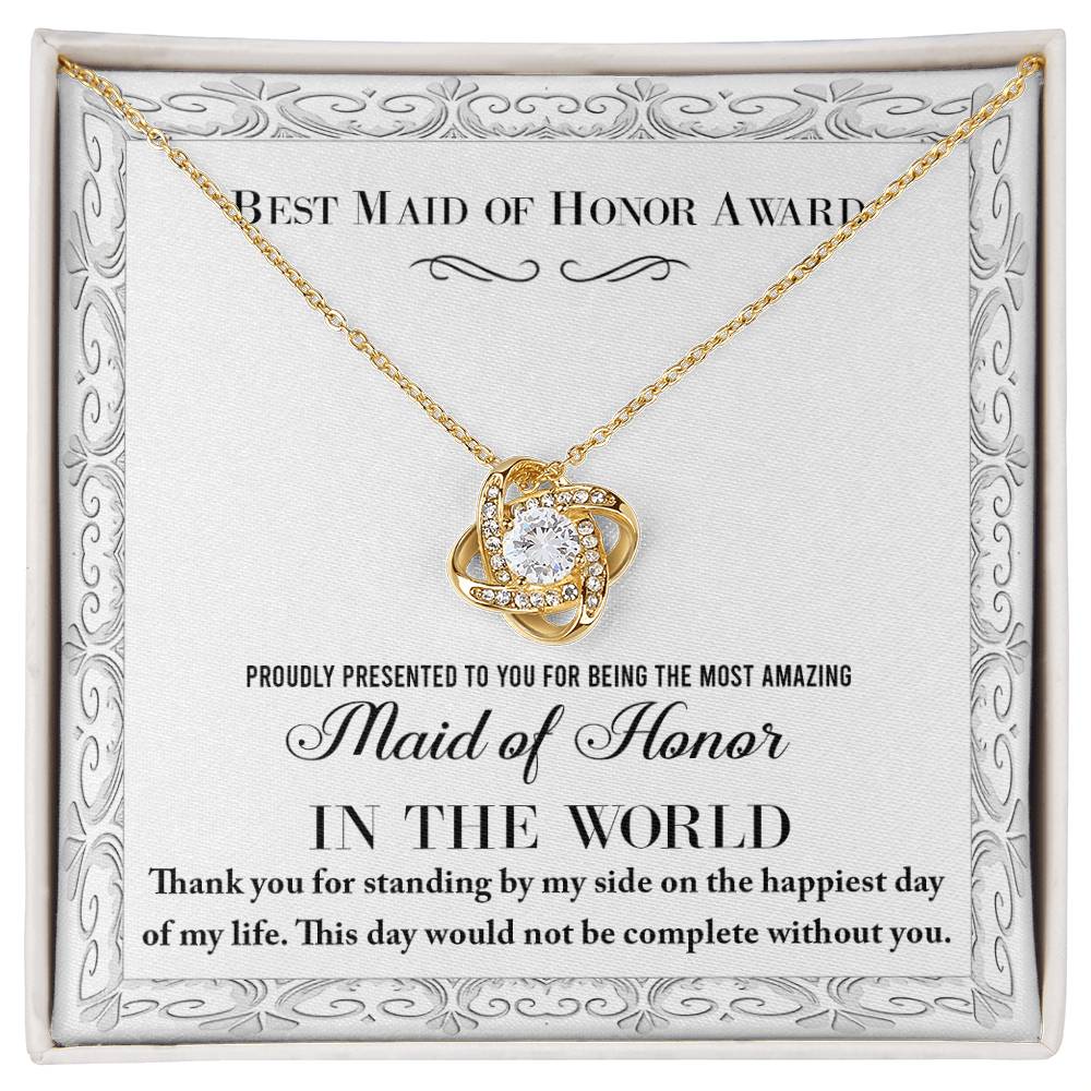 A "To Maid of Honor, Of My Life - Love Knot Necklace," crafted in 14k white gold with a heart-shaped pendant adorned with cubic zirconia crystals, sits elegantly in a jewelry box. The text reads, "Best Maid of Honor Award. Proudly presented to you for being the most amazing Maid of Honor in the world.