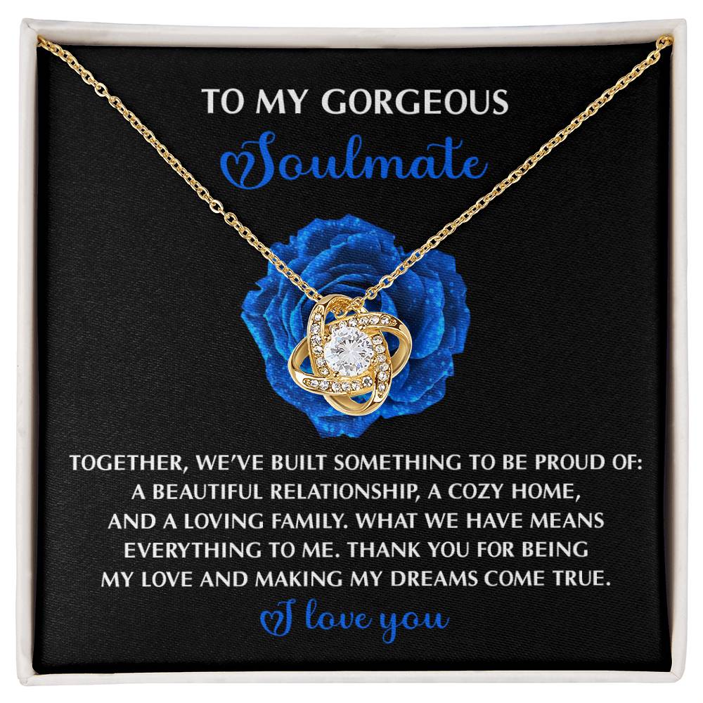 The Soulmate-Dreams Come True - Love Knot Necklace features interlocking rings in white gold, a central cubic zirconia gem, and comes in a box with a touching message next to a blue rose on a black background, radiating elegance and sentiment.