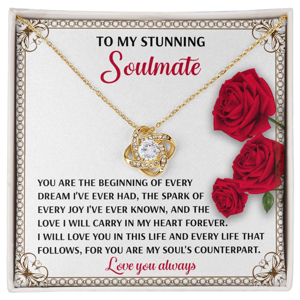 The Soulmate-Soul_s Counterpart - Love Knot Necklace, featuring cubic zirconia and a gold finish, is packaged elegantly in a decorative box with a heartfelt message for your soulmate, surrounded by vibrant red roses.