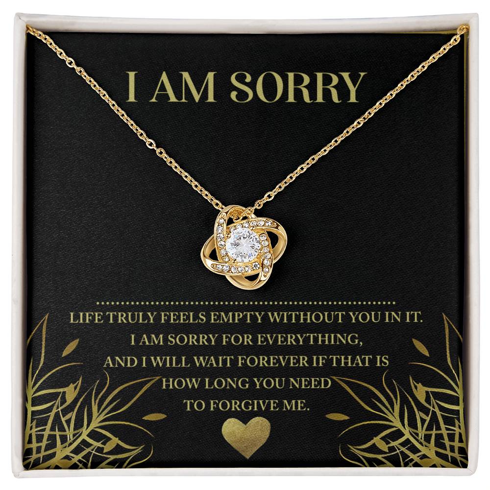 The "Sorry-Without You" Love Knot Necklace, made of gold and featuring a central clear cubic zirconia crystal pendant, is elegantly presented in a box. The background of the box reads, "I AM SORRY" and includes a heartfelt apology message below. This personalized gift eloquently conveys your deep regret.