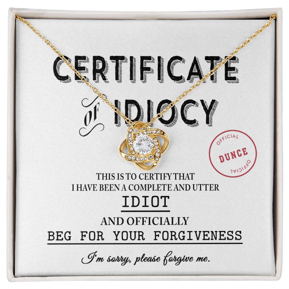 The Sorry-Certificate Of Idiocy - Love Knot Necklace, featuring a heart-shaped pendant adorned with cubic zirconia crystals, is presented on a "Certificate of Idiocy" that states: "I have been a complete and utter idiot and officially beg for your forgiveness.
