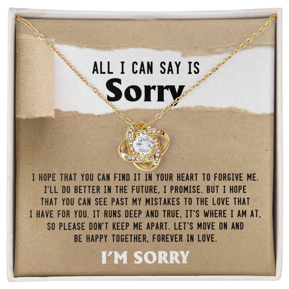 A gold Sorry-Keep Me Apart - Love Knot Necklace featuring a heart-shaped pendant, elegantly presented in a box adorned with cubic zirconia crystals. The package includes a heartfelt apology message titled "All I Can Say Is Sorry," expressing deep regret and a plea for forgiveness.