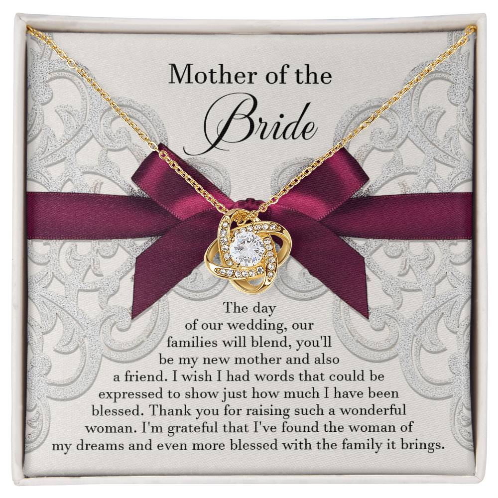 A To Bride's Mom, My New Mother - Love Knot Necklace with a heart pendant, crafted from 14k white gold and adorned with cubic zirconia crystals, is displayed on a decorative card with a maroon ribbon. The card reads, "Mother of the Bride" and contains a heartfelt message of gratitude.