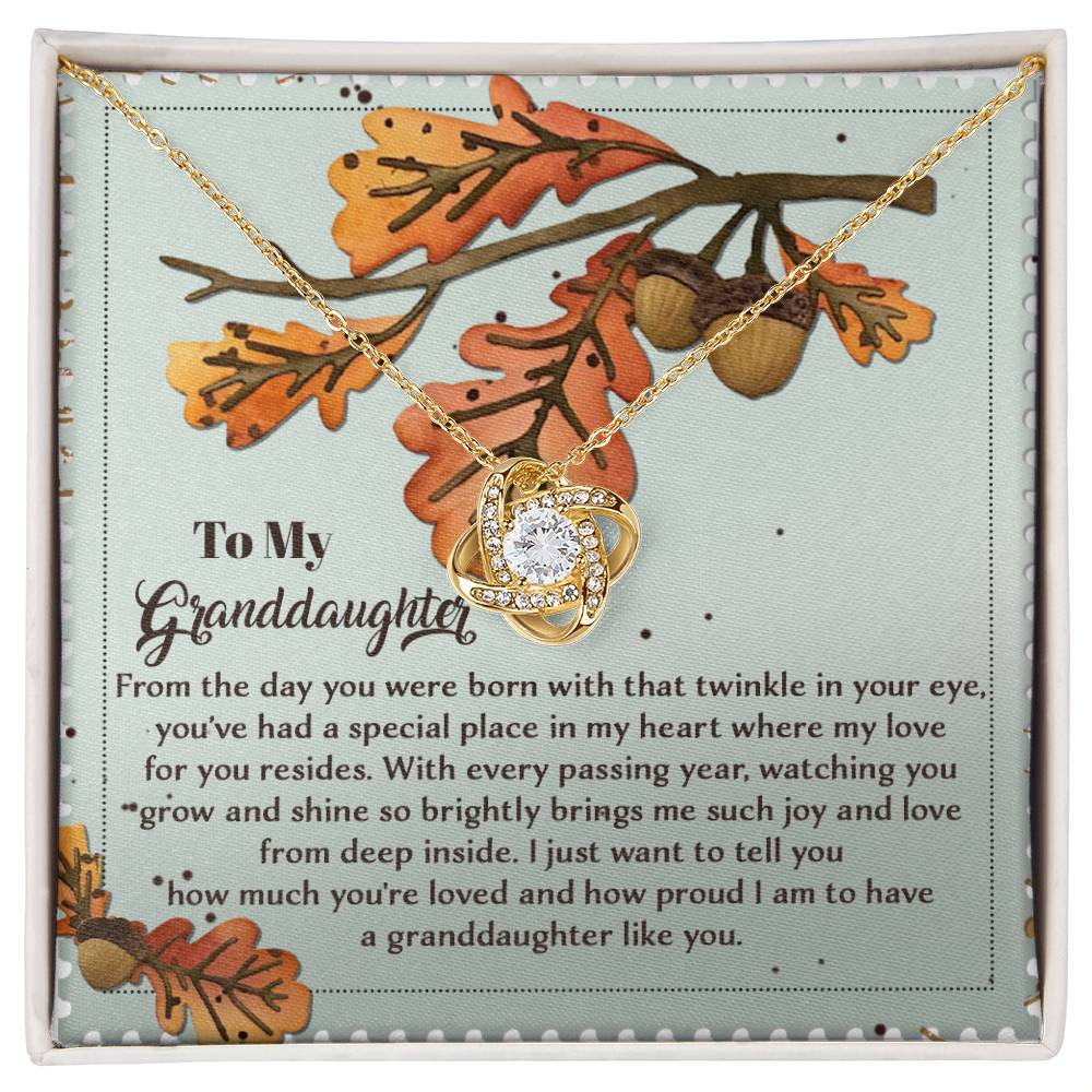 The Granddaughter-From Deep Inside - Love Knot Necklace, featuring a gold pendant, is elegantly displayed on a sentimental gift card adorned with autumn leaves and an acorn design. Embellished with cubic zirconia crystals, this personalized gift beautifully symbolizes the bond between you two.