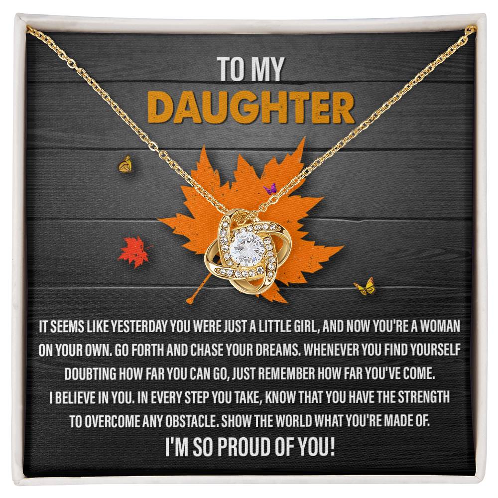 The Daughter-You Can Go - Love Knot Necklace, featuring an interlocking heart and infinity symbol pendant adorned with cubic zirconia crystals, is displayed above a heartfelt message to a daughter on a wooden background with a maple leaf decoration.