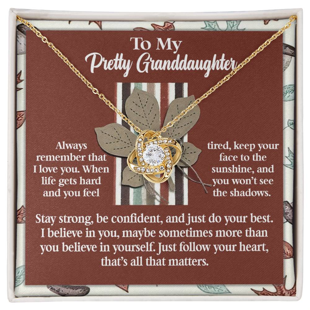 Granddaughter-See The Shadows - Love Knot Necklace, featuring a gold heart-shaped design with a cubic zirconia crystal pendant on a decorative card, complemented by an inspiring message for your granddaughter.