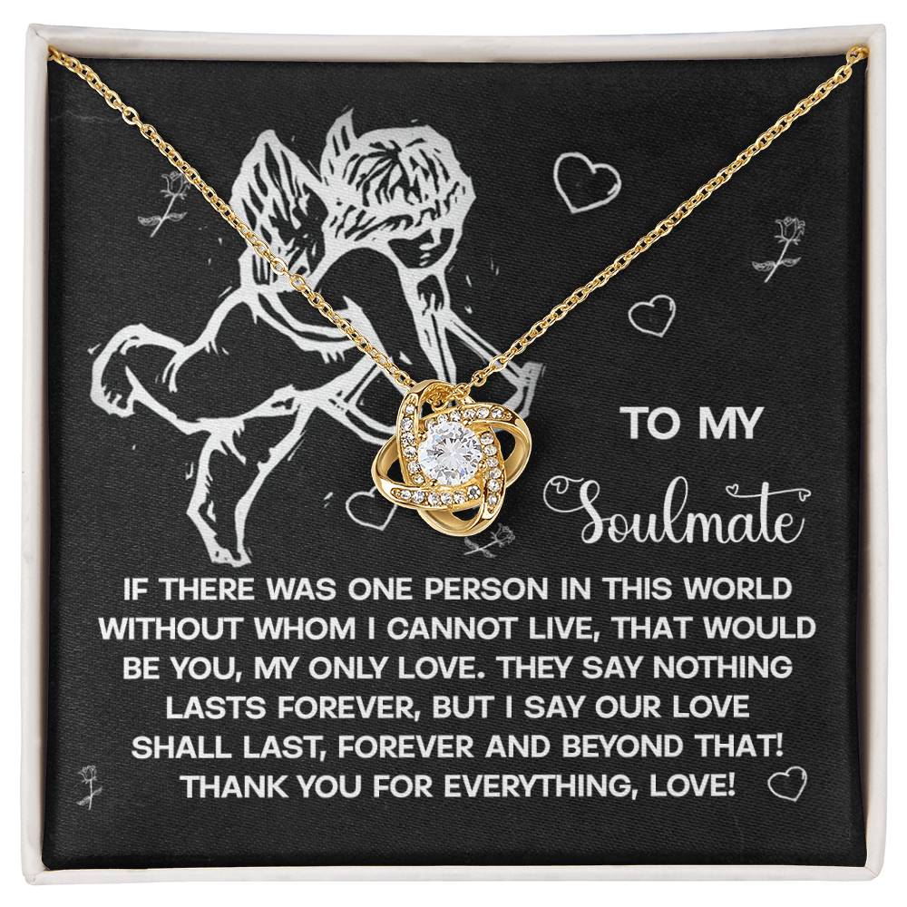 The Soulmate-Lasts Forever Love Knot Necklace features a heart-shaped pendant with sparkling cubic zirconia, showcased in a gift box. A cherub illustration and romantic message to a soulmate appear on the background, all elegantly wrapped in a gold finish.