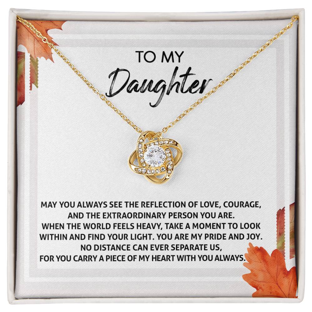 The Daughter-Find Your Light - Love Knot Necklace features a heart-shaped pendant embellished with cubic zirconia crystals, available in either white gold or yellow gold finish. Presented in a display box adorned with an autumn leaf design, it includes the heartfelt message "To My Daughter," expressing love, pride, and encouragement.