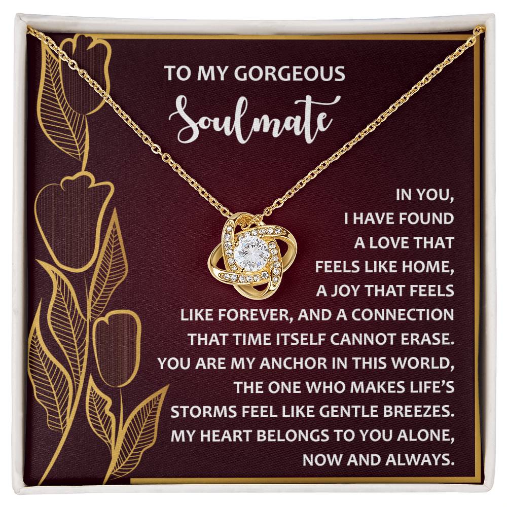 The Soulmate-Gentle Breezes Love Knot Necklace, embellished with cubic zirconia crystals, is presented in an ornate box with sentimental text against a luxurious maroon and gold floral backdrop.