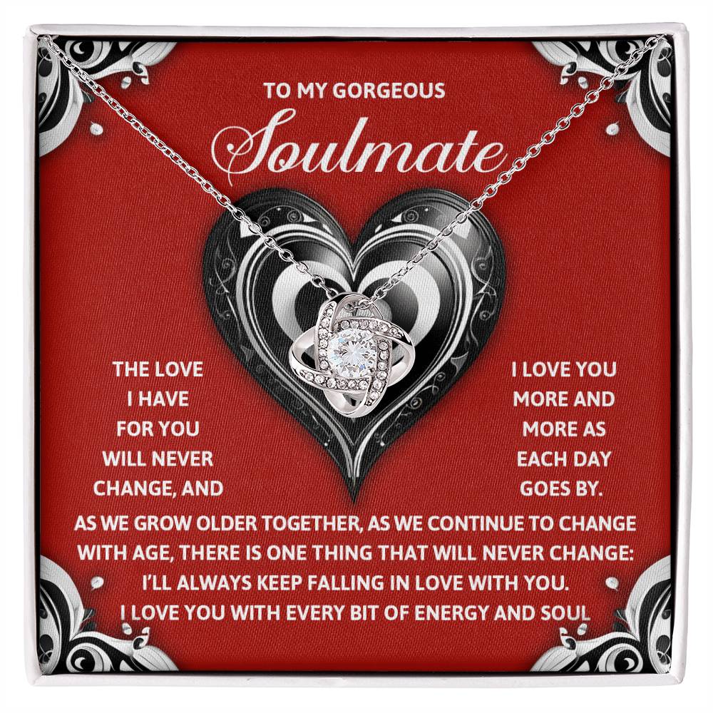 Surprise your soulmate with the Soulmate-Energy And Soul - Love Knot Necklace. This stunning pendant, adorned with cubic zirconia crystals, comes in a gift box against a romantic red background with heart designs, delivering a personalized message of love.