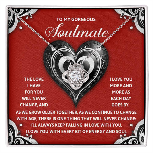 Surprise your soulmate with the Soulmate-Energy And Soul - Love Knot Necklace. This stunning pendant, adorned with cubic zirconia crystals, comes in a gift box against a romantic red background with heart designs, delivering a personalized message of love.