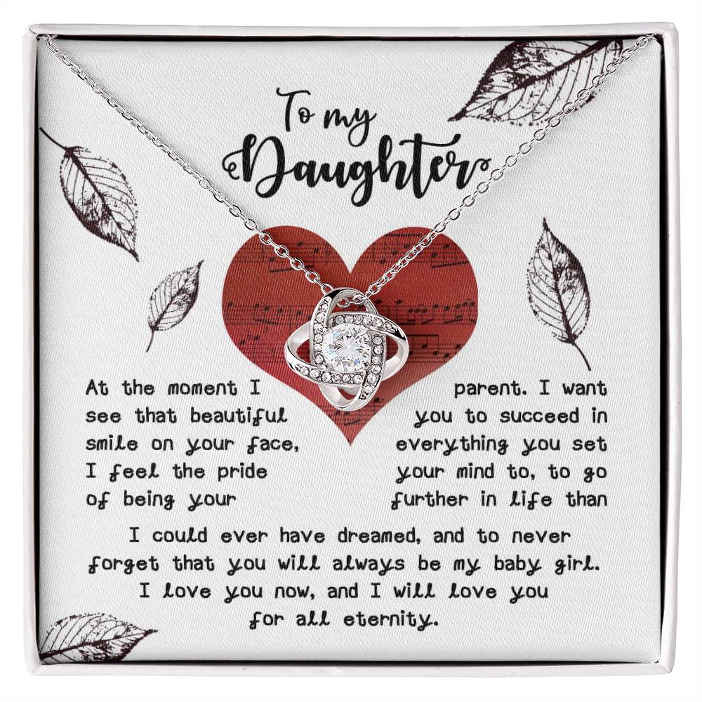 The Daughter-On Your Face - Love Knot Necklace, featuring an intertwined design embellished with cubic zirconia crystals, is beautifully presented in a box with a heartfelt message to your daughter, surrounded by leaf illustrations and set against a musical note background.