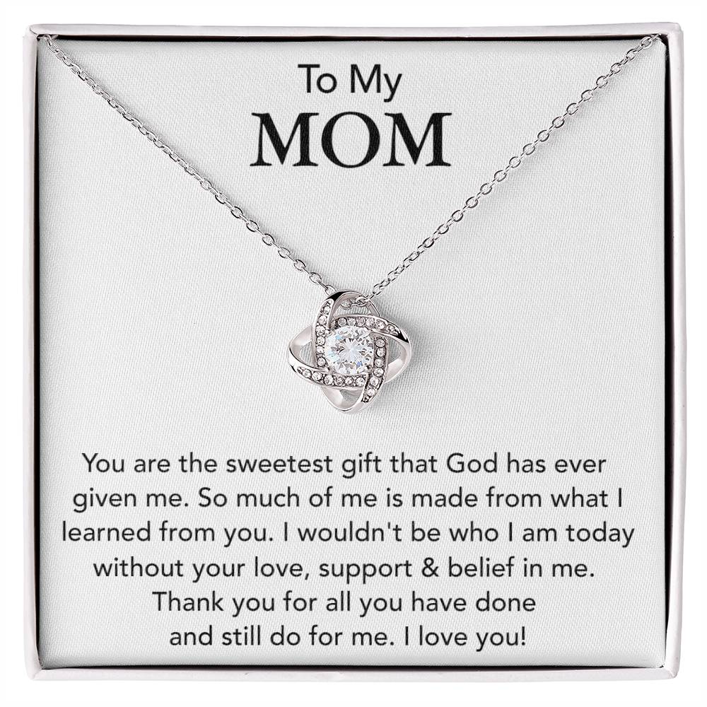A "To My Mom, You Are The Sweetest Gift That God Has Ever Given Me" love knot necklace with a heart-shaped pendant encrusted with cubic zirconia crystals is displayed in a box, accompanied by a message to a mother expressing gratitude and love from ShineOn Fulfillment.