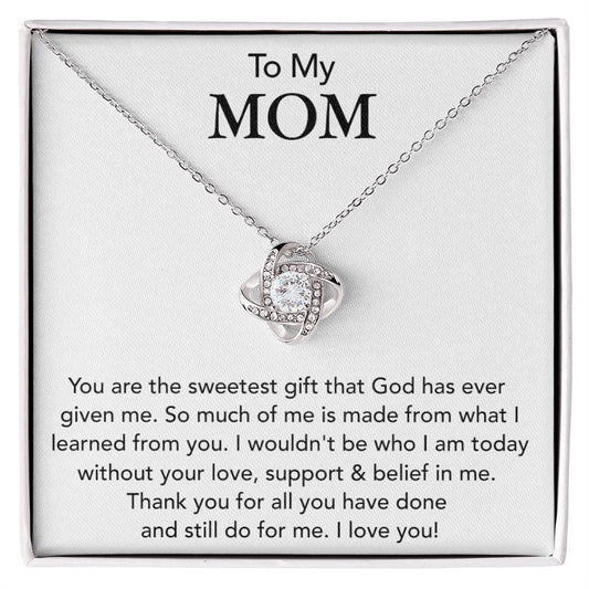 A "To My Mom, You Are The Sweetest Gift That God Has Ever Given Me" love knot necklace with a heart-shaped pendant encrusted with cubic zirconia crystals is displayed in a box, accompanied by a message to a mother expressing gratitude and love from ShineOn Fulfillment.