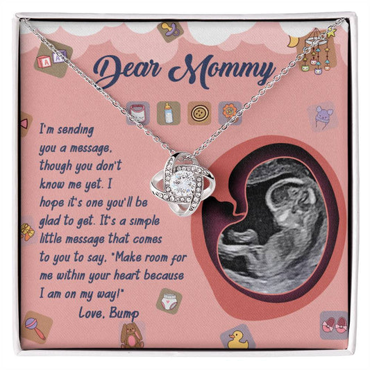 The "To Mom To Be, On My Way - Love Knot Necklace" is a perfect personalized gift, featuring a beautiful necklace in a gift box with the heartfelt message "Dear Mommy," alongside an ultrasound image of a baby. The stunning Love Knot Necklace is adorned with cubic zirconia crystals.