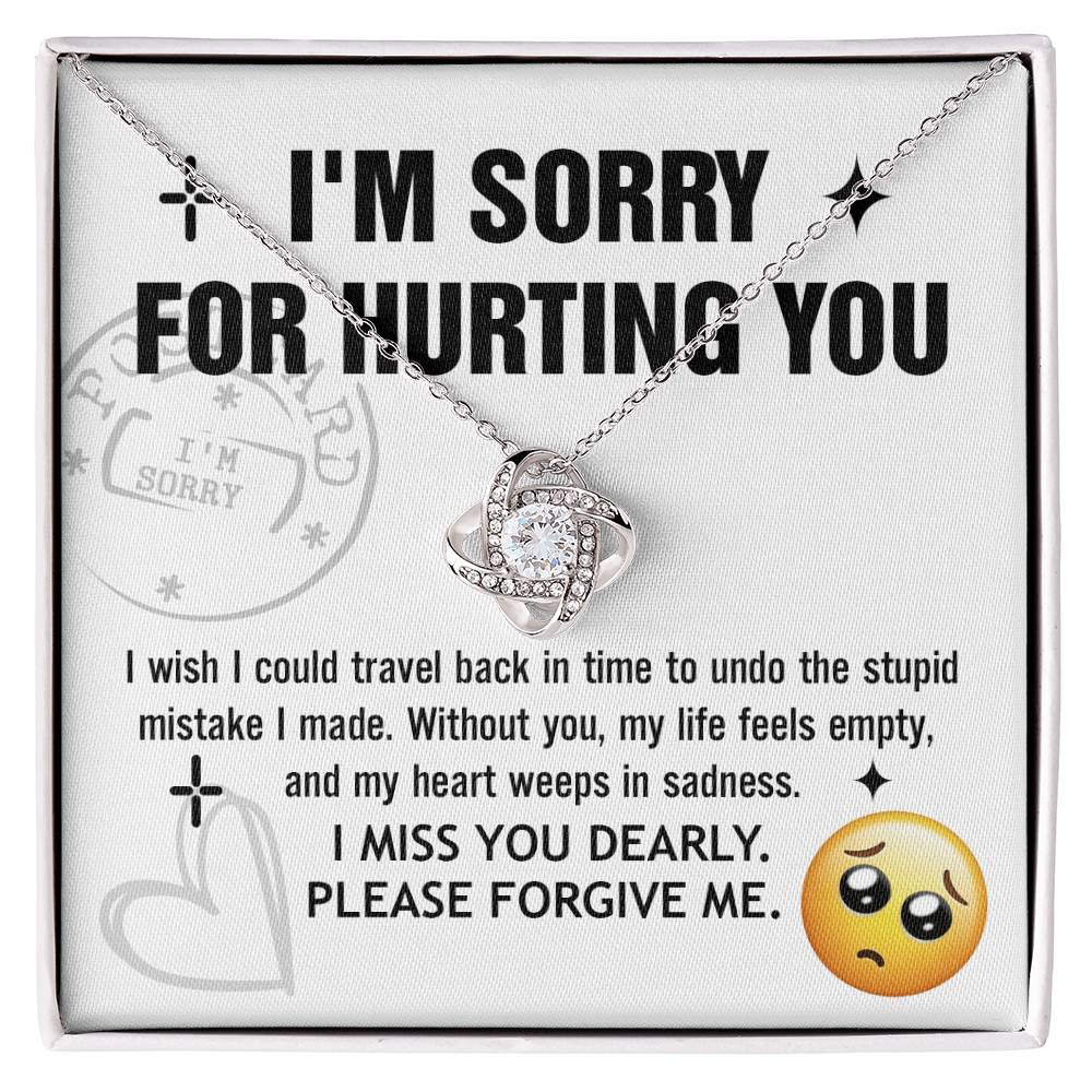 A Sorry-Travel Back - Love Knot Necklace with a white gold finish is displayed on a card featuring the text: "I'M SORRY FOR HURTING YOU," along with an apology note and a sad face emoji at the bottom right.
