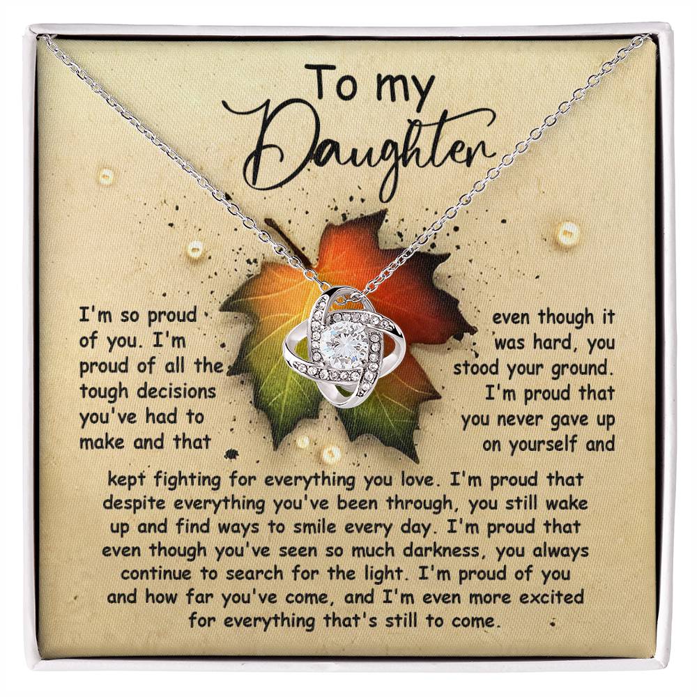 The Daughter-Stood Your Ground - Love Knot Necklace features an infinity heart pendant on a chain, beautifully presented in a box embellished with cubic zirconia crystals and a heartfelt message. The background leaf design thoughtfully frames the words of pride and encouragement for a daughter, making it the perfect personalized gift.
