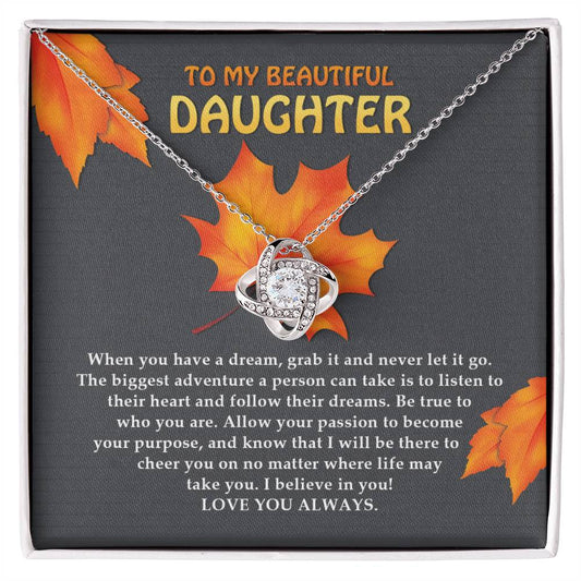 The "Daughter-To Their Heart - Love Knot Necklace" features a heart-shaped pendant, meticulously crafted from 14k white gold and set with dazzling Cubic Zirconia Crystals. Displayed in a box beside a heartfelt message to a daughter and surrounded by autumn leaves, this necklace is truly captivating.
