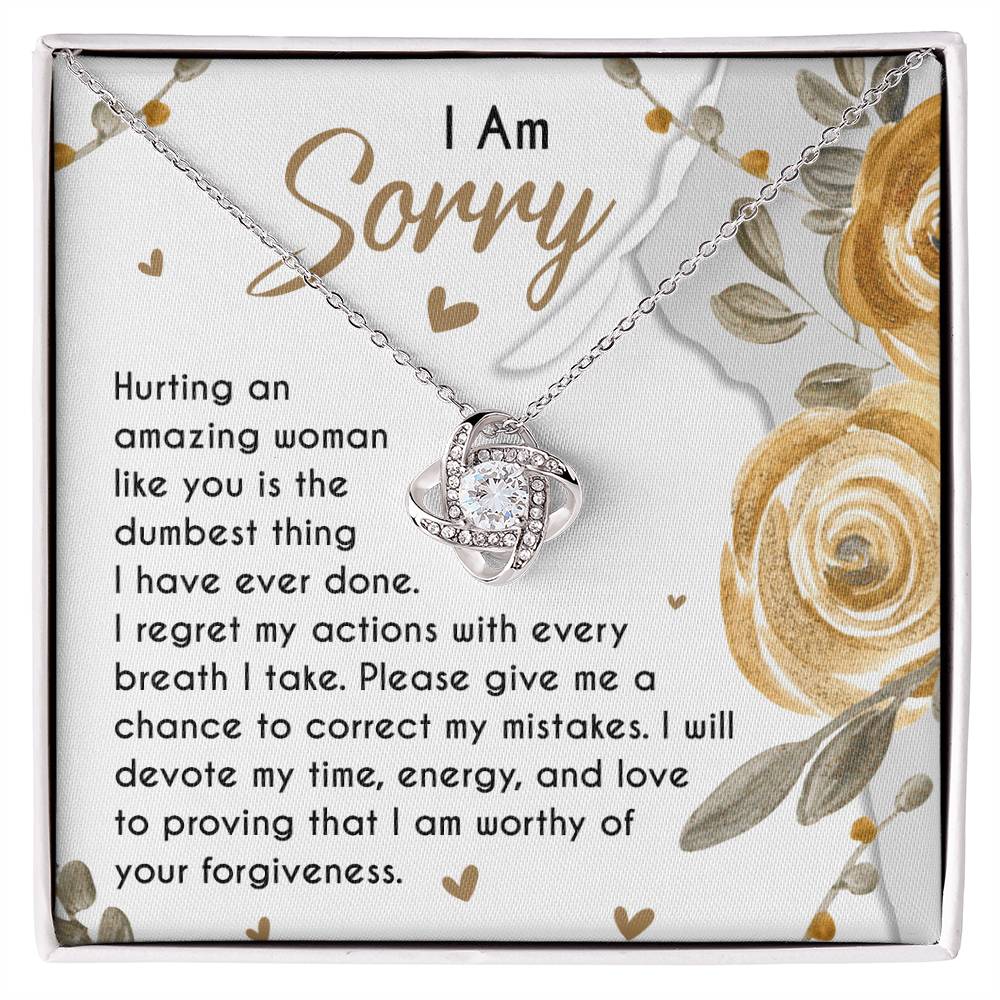 The Sorry-Amazing Woman - Love Knot Necklace, adorned with cubic zirconia crystals, rests in a jewelry box on a heartfelt note that reads, "I Am Sorry. Hurting an amazing woman like you is the dumbest thing I have ever done..." along with more apologetic text.