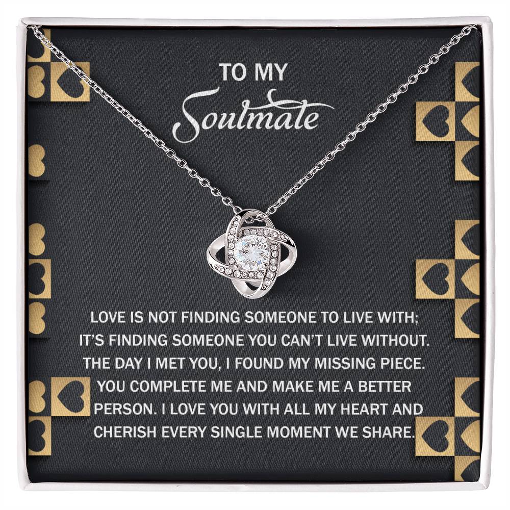 The Soulmate-Missing Piece Love Knot Necklace is a silver heart with an entwined design and gold finish, presented on a black card with gold heart accents and a sentimental message about love and soulmates celebrating their timeless bond.