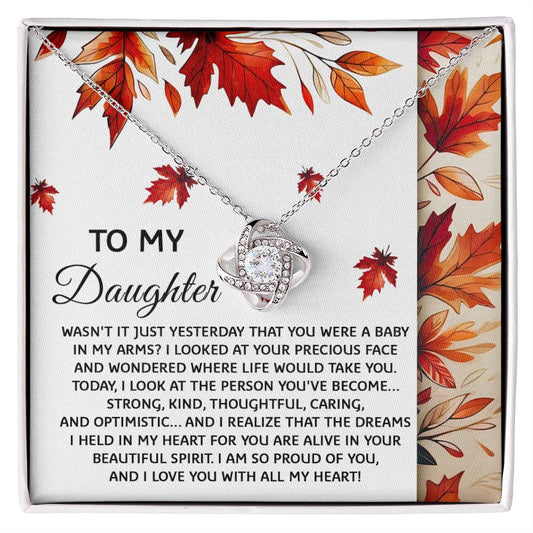 The "Daughter-Were A Baby - Love Knot Necklace," presented in a gift box with a heartfelt message to a daughter, is adorned with cubic zirconia crystals and set against an autumn leaves background.
