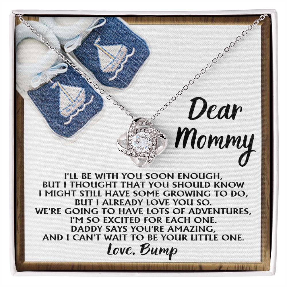 The "To Mom To Be, You're Amazing - Love Knot Necklace," featuring a twisted knot pendant in 14k white gold adorned with cubic zirconia crystals, is presented on a card addressed to "Mommy" from an unborn child, and comes with a pair of baby booties decorated with sailboat designs.