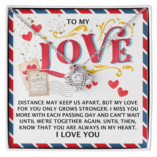 The Soulmate-In My Heart - Love Knot Necklace is displayed on a card with a heartfelt message about distance and affection, featuring colorful text, heart graphics, and shimmering cubic zirconia crystals. It is also available in 14k white gold for an elegant touch.