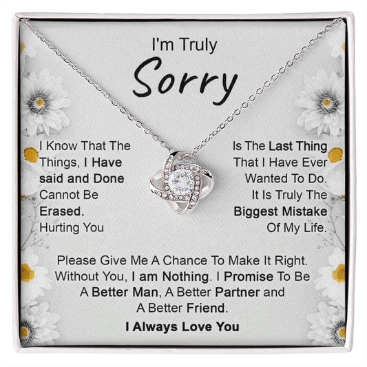 The "I’m Truly Sorry - Love Knot Necklace," featuring a pendant adorned with cubic zirconia crystals, rests on a heartfelt message that reads, "I'm Truly Sorry." The text conveys remorse for past actions and a commitment to becoming a better person, partner, and friend. The background is decorated with delicate floral designs.