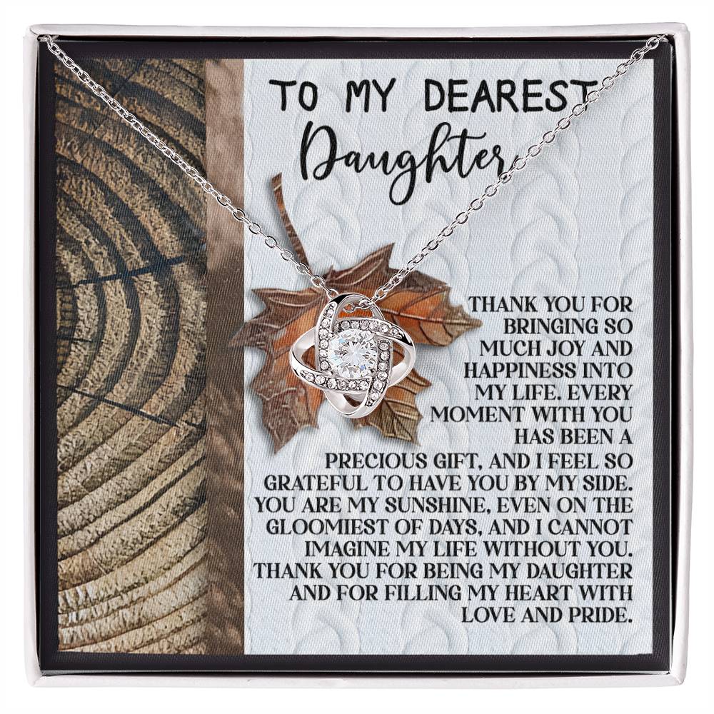 The Daughter-Love And Pride - Love Knot Necklace showcases a beautiful gold finish adorned with cubic zirconia crystals. It comes displayed on a card with the heartfelt message "To My Dearest Daughter," expressing love, gratitude, and the joy she brings.