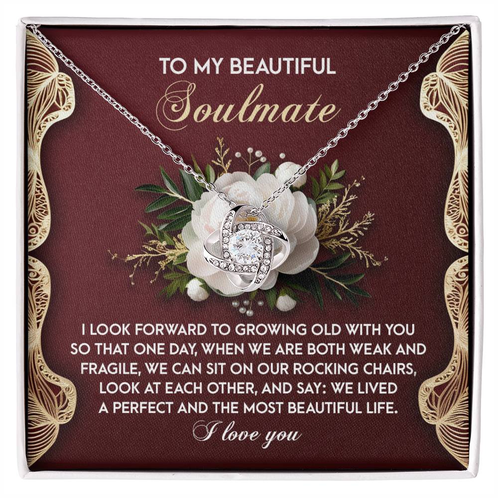 The Soulmate-Rocking Chairs Love Knot Necklace in white gold features a floral design with cubic zirconia, displayed on a red card with gold accents and a heartfelt message about love and growing old together.