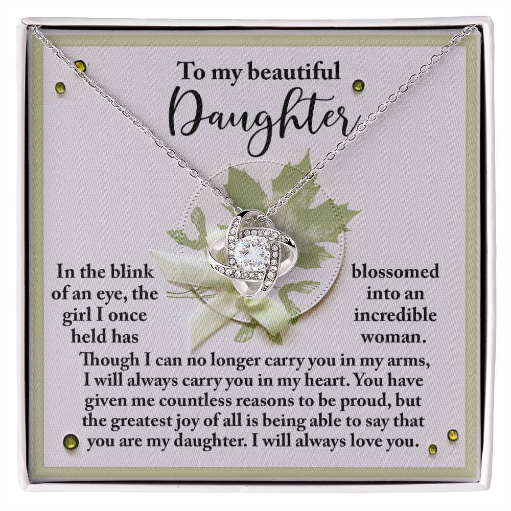 A silver Love Knot necklace, adorned with sparkling cubic zirconia crystals, is displayed on a card that reads: "To my beautiful daughter, In the blink of an eye, the girl I once held has blossomed into an incredible woman...