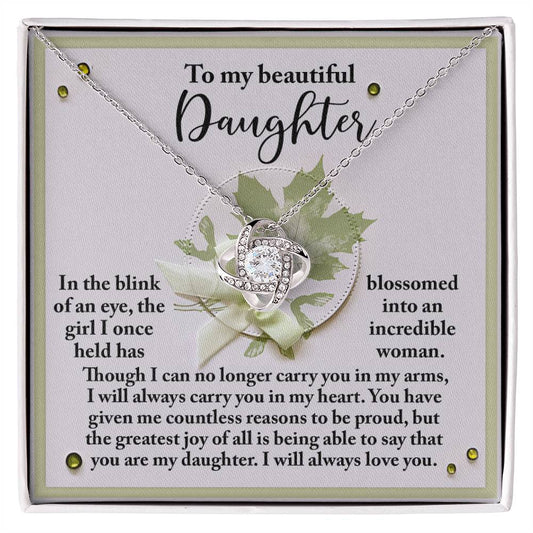 A silver Love Knot necklace, adorned with sparkling cubic zirconia crystals, is displayed on a card that reads: "To my beautiful daughter, In the blink of an eye, the girl I once held has blossomed into an incredible woman...