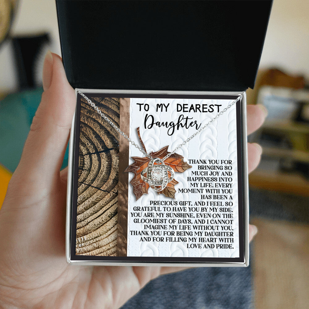 A hand holding a personalized gift box featuring the Daughter-Love And Pride - Love Knot Necklace, adorned with cubic zirconia crystals and accompanied by a heartfelt message for a daughter, symbolizing the love and joy she brings to their life.