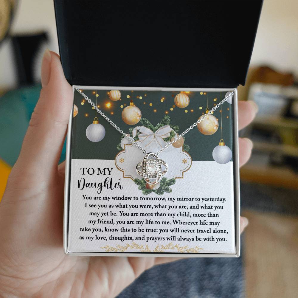 In the background, festive lights cast a warm glow as someone opens a jewelry box to reveal the Daughter-My Mirror - Love Knot Necklace. This exquisite piece, embellished with shimmering cubic zirconia crystals, comes with a heartfelt message for a daughter, making it a truly special and personalized gift.