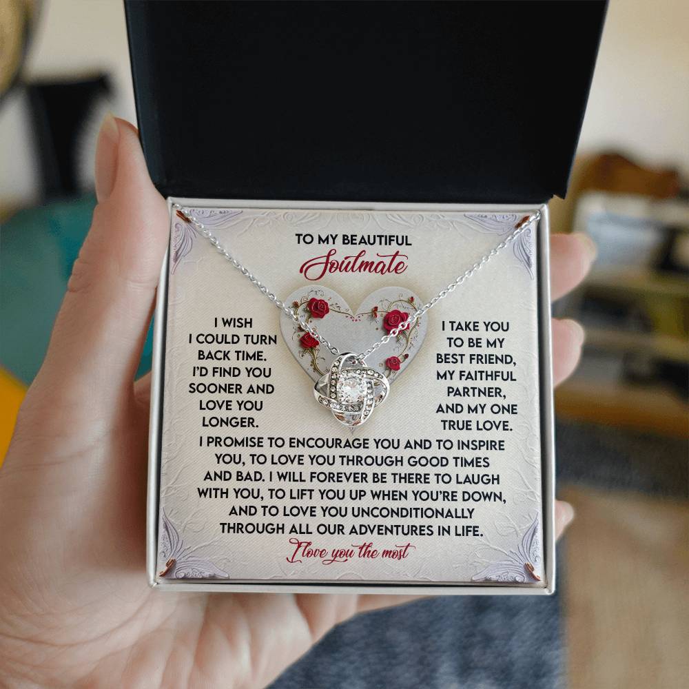 A person holds a jewelry box open, displaying the Soulmate-Laugh With You - Love Knot Necklace featuring a heart-shaped pendant adorned with cubic zirconia crystals. Inside the lid, there's a heartfelt message for a "beautiful soulmate.