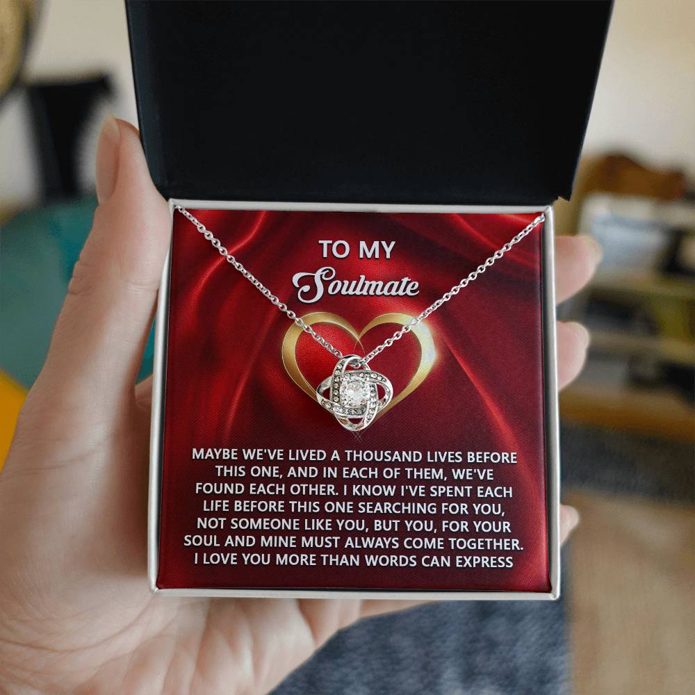 A hand holds the Soulmate-Your Soul - Love Knot Necklace, crafted from silver with cubic zirconia, above a card titled "To My Soulmate" and embellished with a heart graphic.