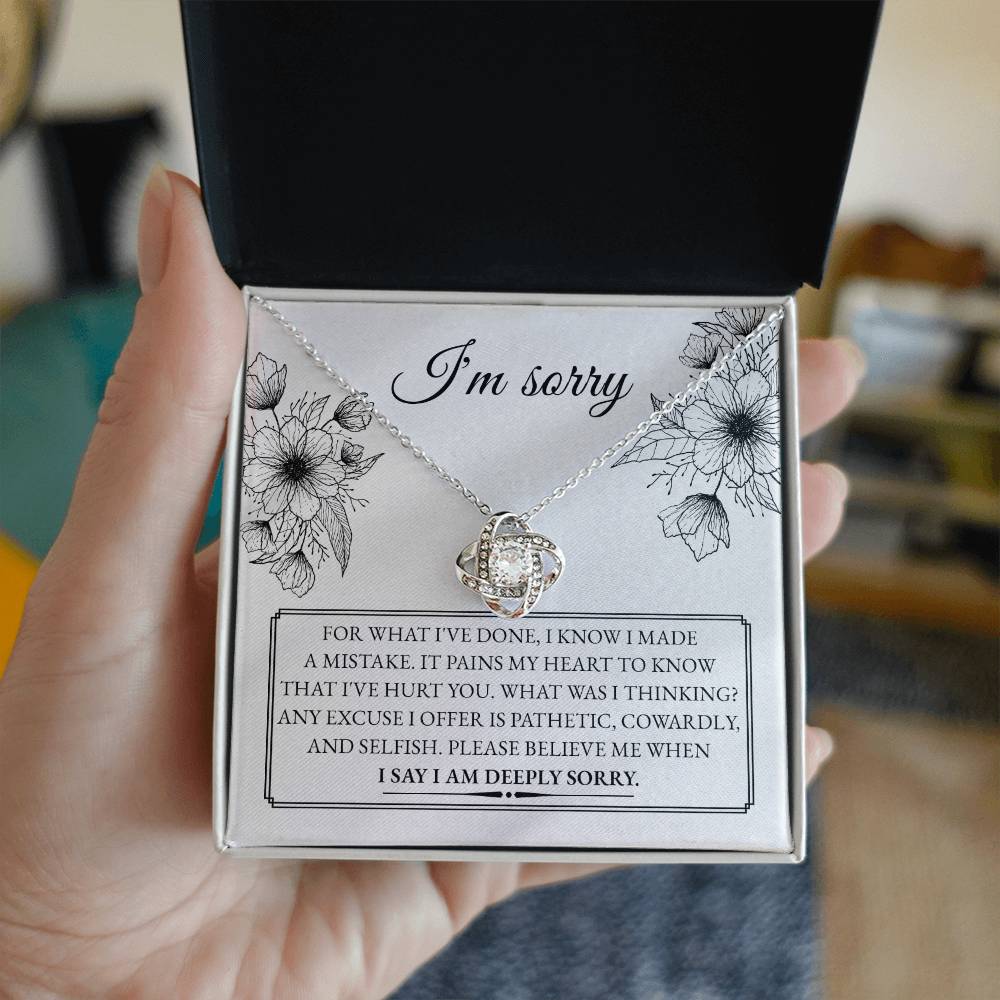 A "Sorry-Made A Mistake - Love Knot Necklace" features a box with a heartfelt apology message. The white gold finish and cubic zirconia crystals shimmer, as the text expresses deep regret and sorrow for causing hurt, describing the actions as pathetic, cowardly, and selfish, pleading for forgiveness.