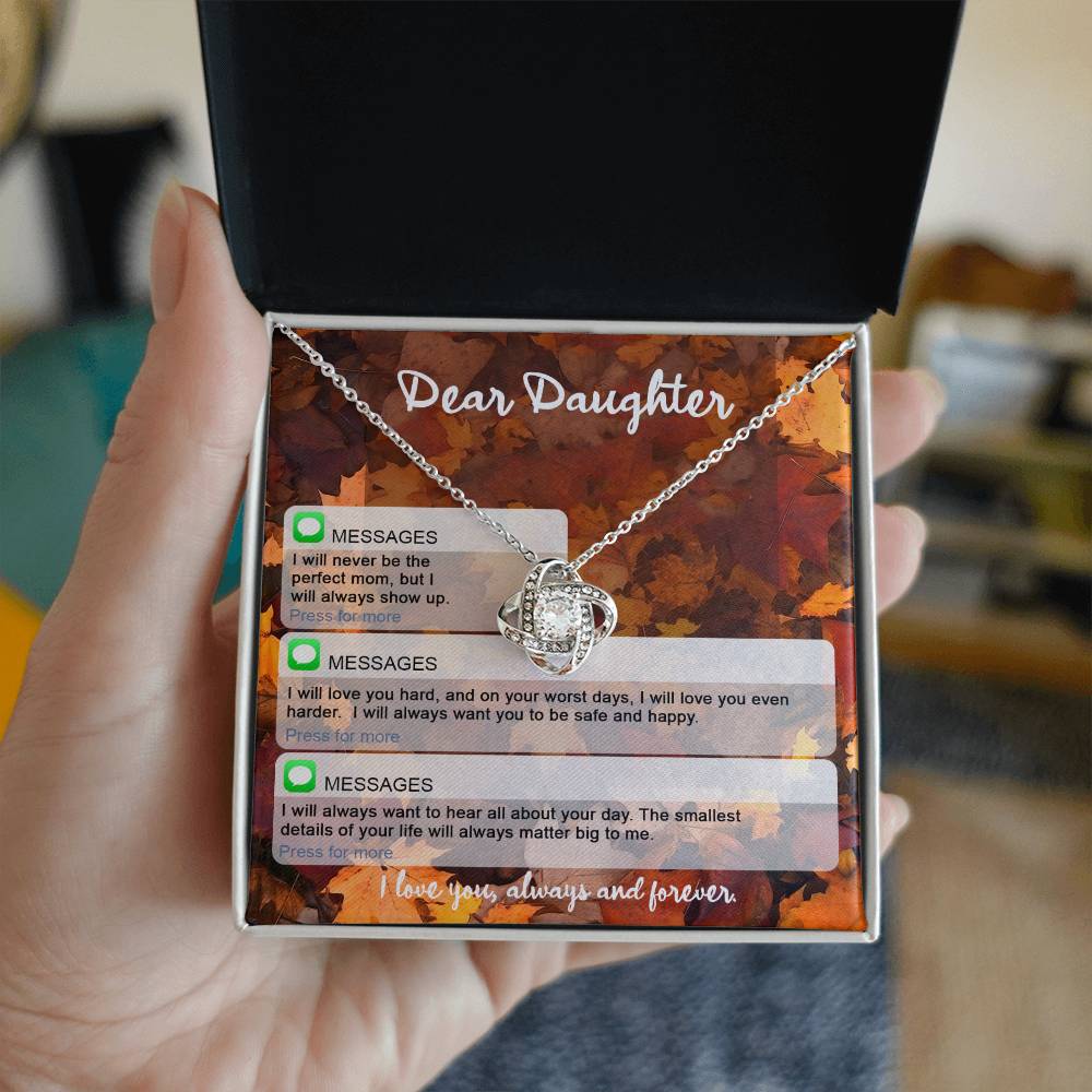 A hand holds an open jewelry box containing a beautiful Daughter-Perfect Mom - Love Knot Necklace adorned with cubic zirconia crystals. The pendant features a letter to a daughter, filled with heartfelt messages and a closing sentiment of eternal love, making it the perfect personalized gift.