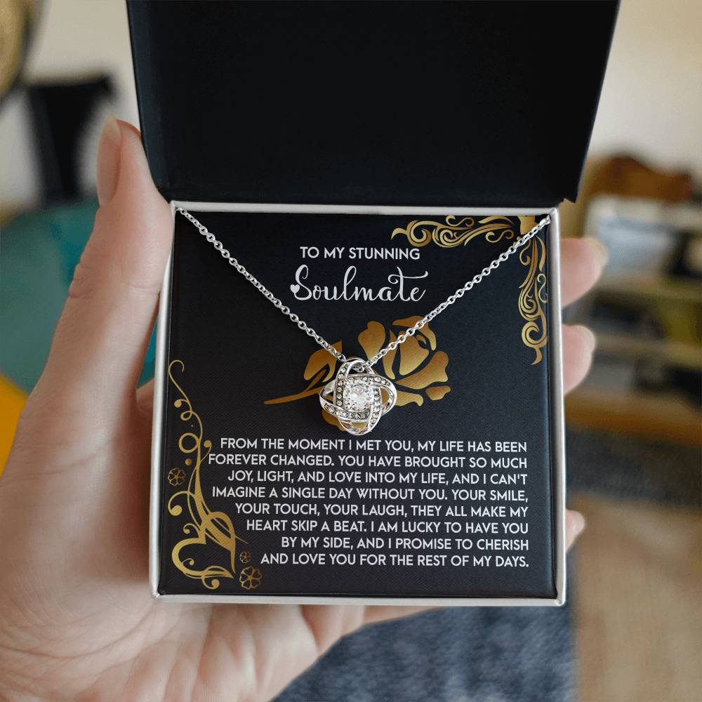 A hand holds an open box featuring the "Soulmate-I Met You 2 - Love Knot Necklace" adorned with cubic zirconia crystals. The box displays a heartfelt message, "To my stunning soulmate," complemented by a personalized note, creating an ideal personalized gift for a cherished loved one.