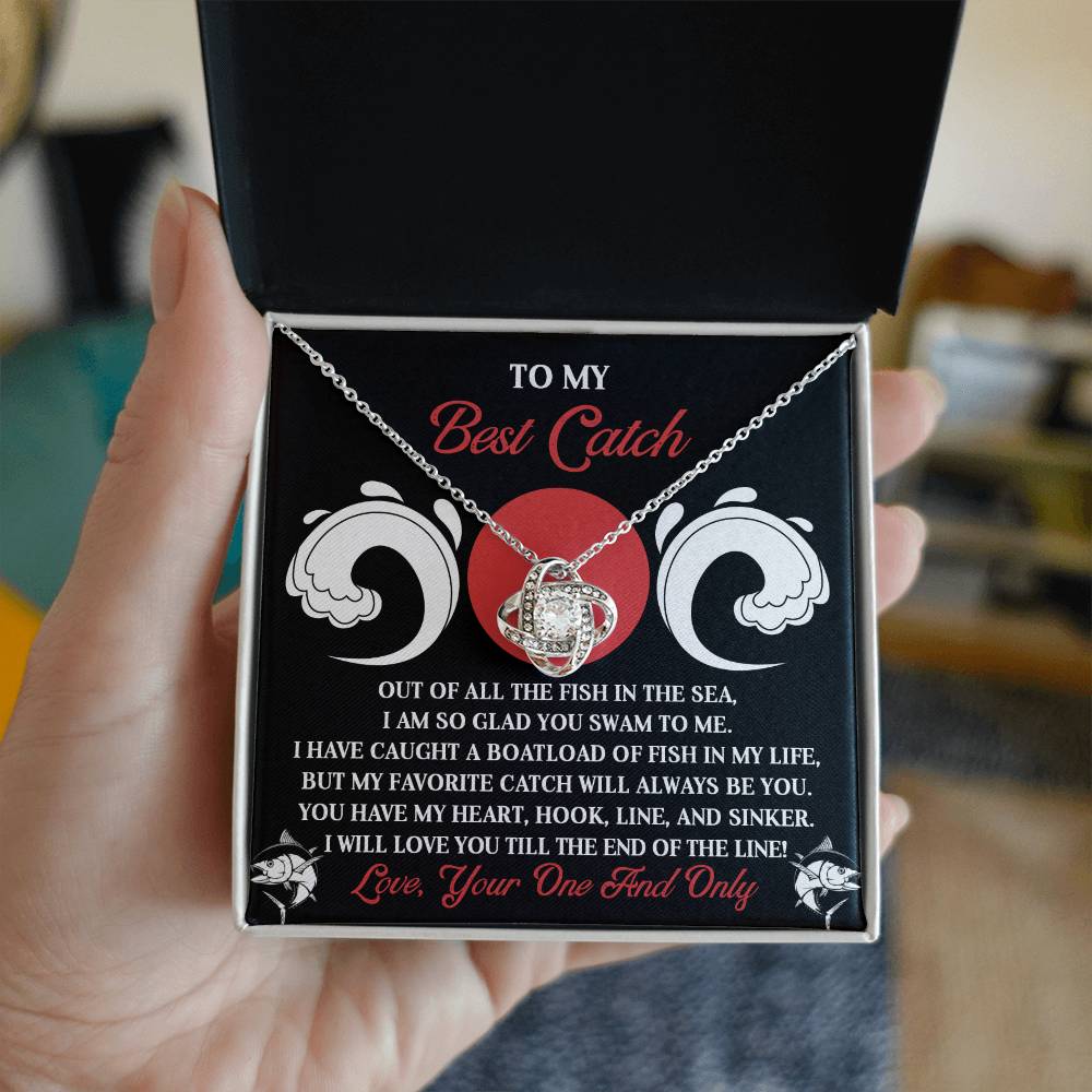 A hand holds the Soulmate-Of The Line - Love Knot Necklace box, revealing a heart-shaped pendant adorned with sparkling cubic zirconia crystals. The box includes a romantic message, making it an ideal personalized gift.