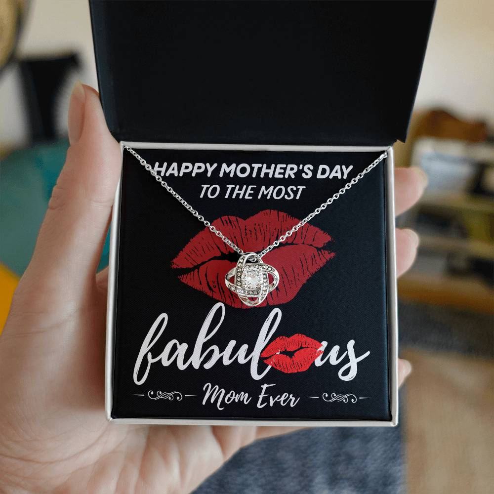 A hand holds an open jewelry box containing the exquisite "To Mom, The Most Fabulous - Love Knot Necklace" adorned with cubic zirconia crystals. The box is inscribed with the message "Happy Mother's Day to the most fabulous Mom ever" and features red lips graphics, making it the perfect personalized gift.