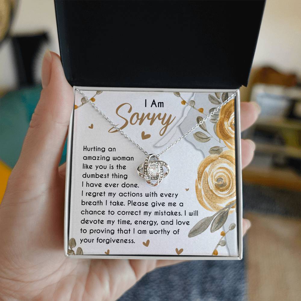 The Sorry-Amazing Woman - Love Knot Necklace, adorned with cubic zirconia crystals, rests in a jewelry box on a heartfelt note that reads, "I Am Sorry. Hurting an amazing woman like you is the dumbest thing I have ever done..." along with more apologetic text.