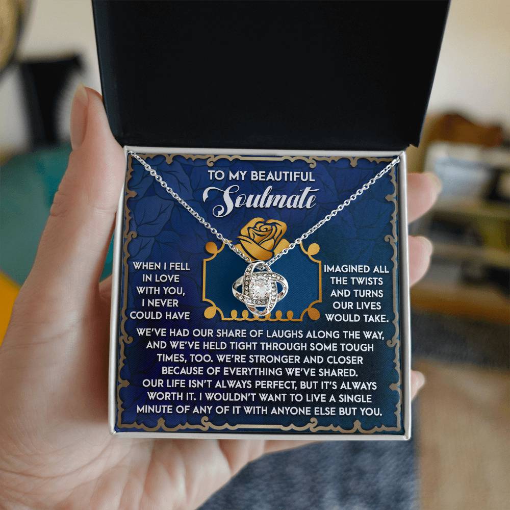 A hand holds an open jewelry box showcasing a beautiful Soulmate-The Way - Love Knot Necklace with cubic zirconia crystals. Inside the lid is inscribed: "To My Beautiful Soulmate," with a heartfelt message about love and life, making it an ideal personalized gift.