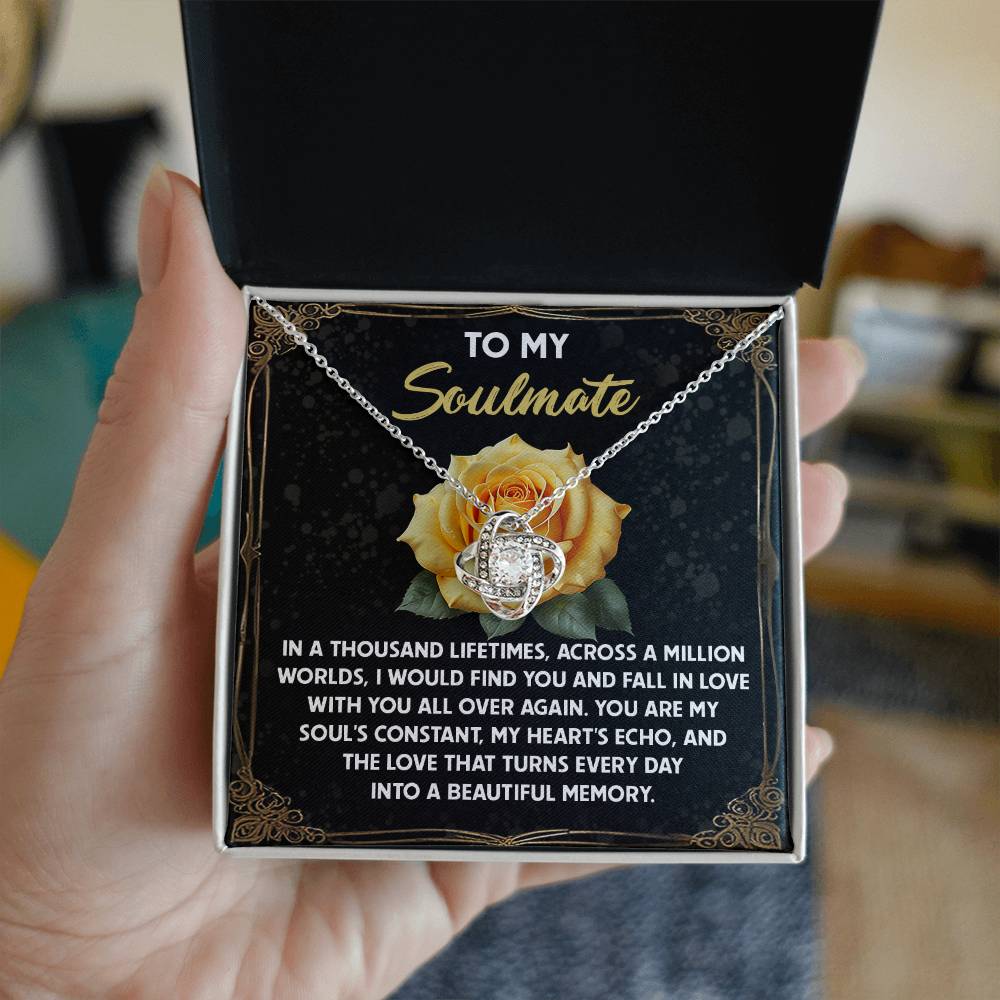 A hand holds an open box showcasing the Soulmate-Beautiful Memory - Love Knot Necklace, adorned with sparkling cubic zirconia crystals. The box reads "To my soulmate" against a rose background, featuring a heartfelt message ideal for a personalized gift.