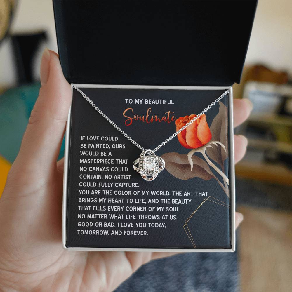 The Soulmate-A Masterpiece - Love Knot Necklace, with a heart-shaped pendant and sparkling cubic zirconia crystals, is beautifully displayed in an open black box adorned with floral design and sentimental text, making it an ideal personalized gift.