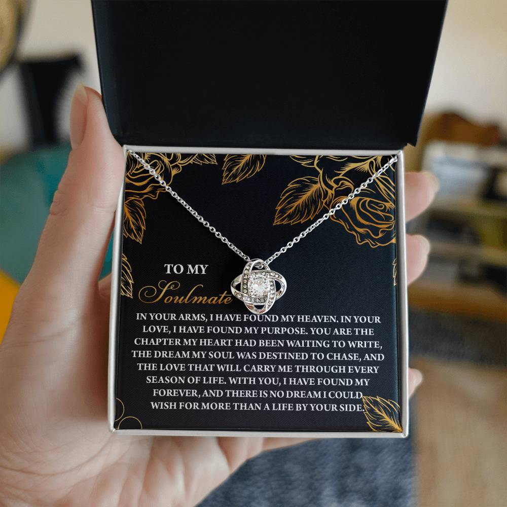 A person holds an open jewelry box displaying the Soulmate-By Your Side Love Knot Necklace, featuring a silver chain and sparkling cubic zirconia crystals, with a romantic message for a soulmate inscribed inside the lid.