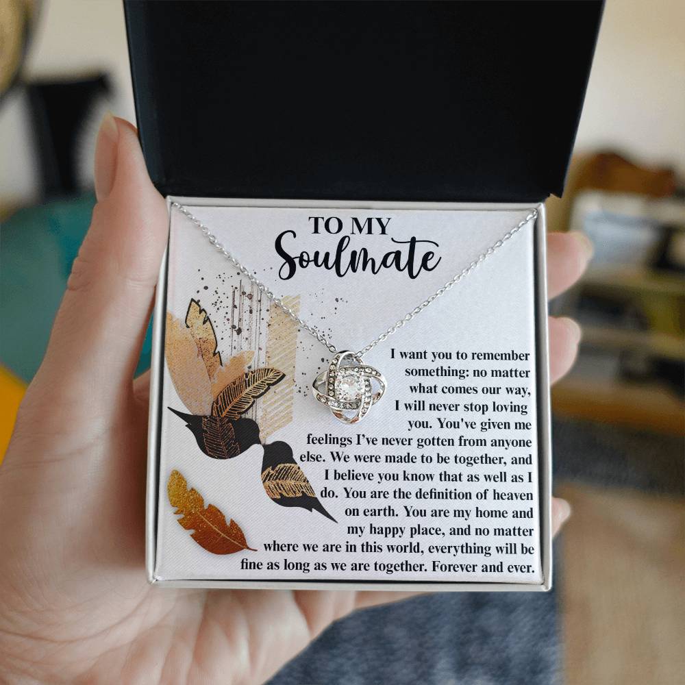 A hand holds an open jewelry box displaying the Soulmate-Given Me Feelings - Love Knot Necklace, adorned with cubic zirconia crystals, and an insert card titled "To My Soulmate," containing a heartfelt message.