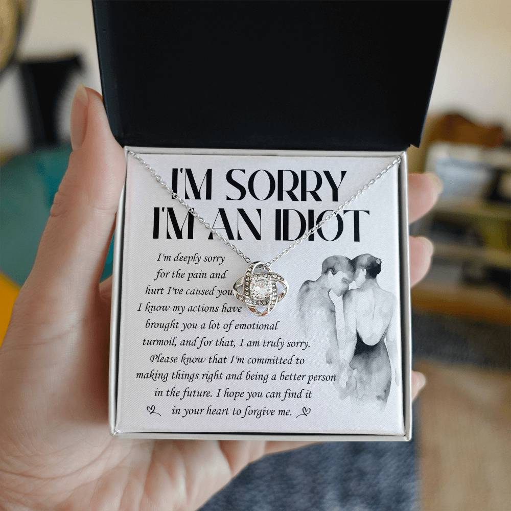 The Sorry-Emotional Turmoil - Love Knot Necklace features a heart-shaped pendant adorned with cubic zirconia crystals and comes presented on a card that reads "I'M SORRY I'M AN IDIOT" along with an apology message, accompanied by an illustration of a couple embracing. This elegant necklace is available in either white gold or yellow gold finish.