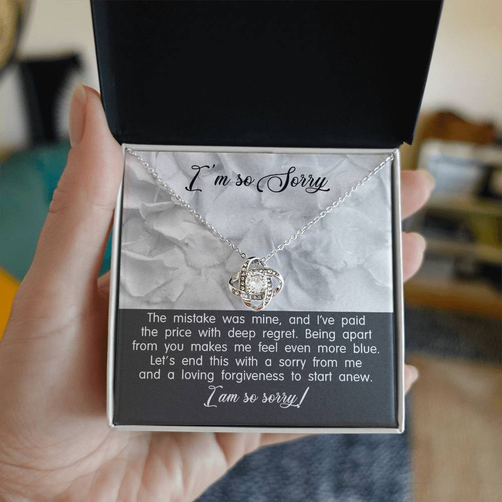 A Sorry-With Deep Regret - Love Knot Necklace with a white gold finish and a pendant on a card that says "I'm so Sorry." The card contains an apology message expressing regret and a plea for forgiveness.
